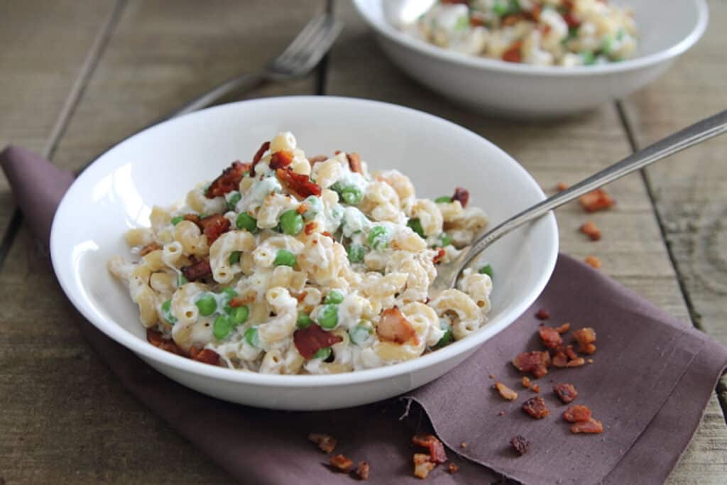 Greek yogurt mac and cheese with peas and bacon in a white bowl.