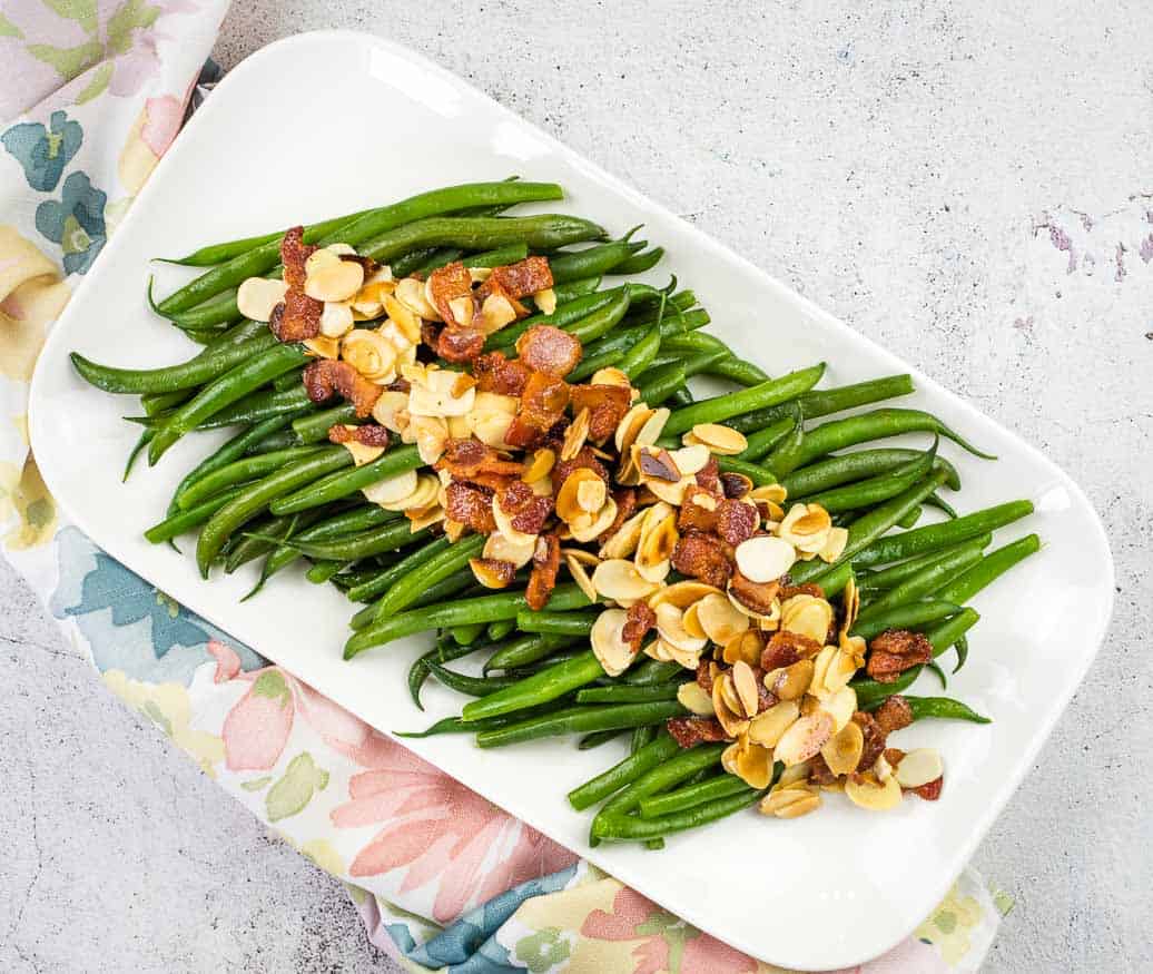 Green beans with almonds and bacon on a white plate.