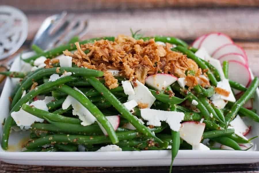 Green beans topped with crunchy onions on a white plate.