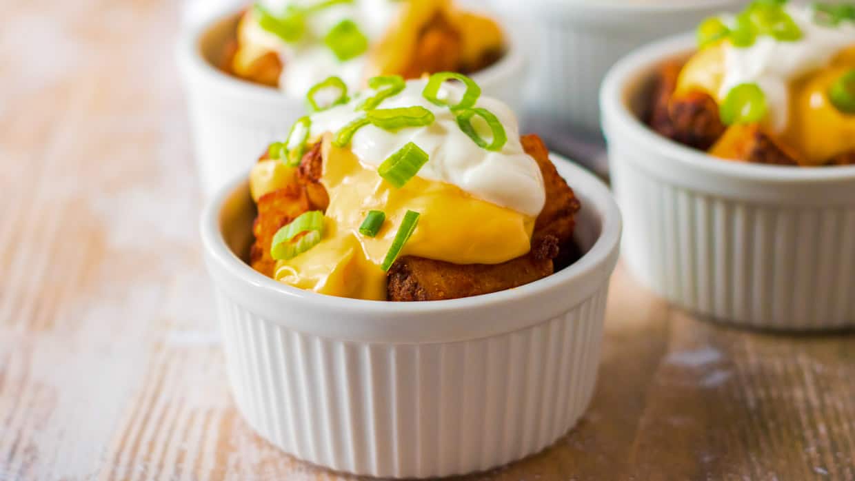 Cheesy Fiesta Potatoes in a white ramekin topped with sour cream and green onions.