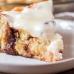 Slice of cinnamon roll pie with cream cheese icing on a white plate.