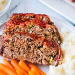 Two slices of meatloaf on a plate with mashed potatoes and carrots.