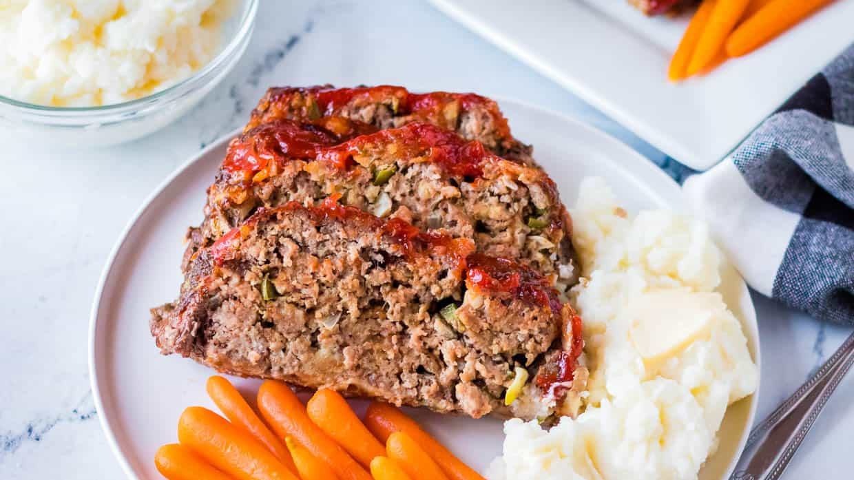 Two slices of meatloaf on a plate with mashed potatoes and carrots.