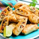 Plate of southwest egg rolls cut open to show the filling of beans, chicken, corn and cheese.