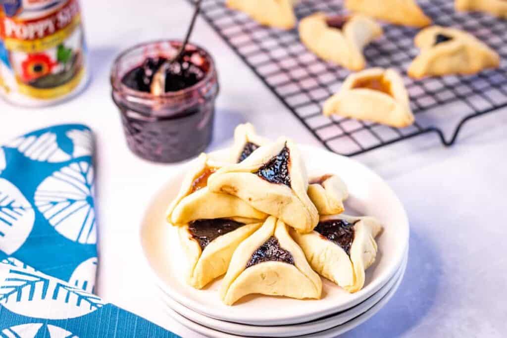 Hamentashen cookies with fruit fillings on a stack of plates.
