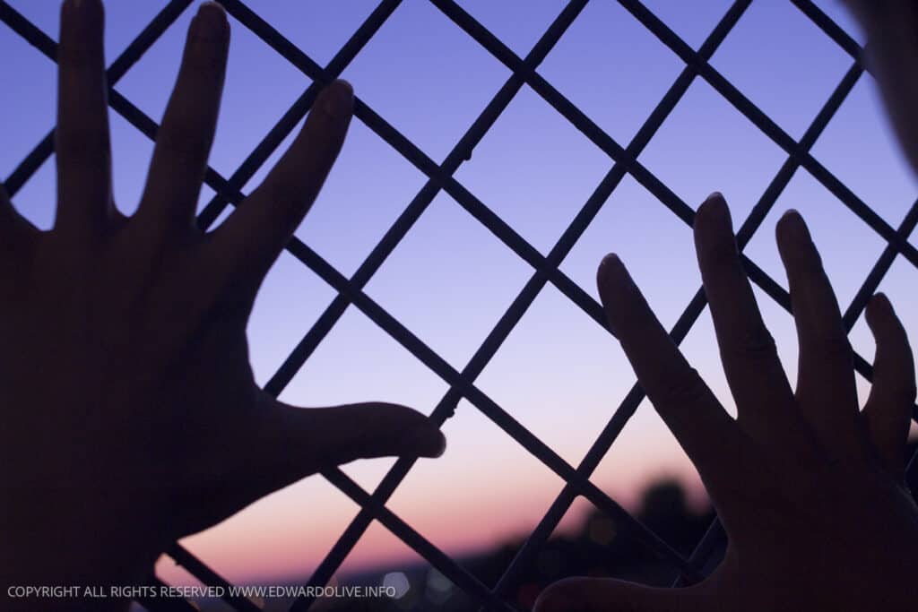 Hands against a prison fence.