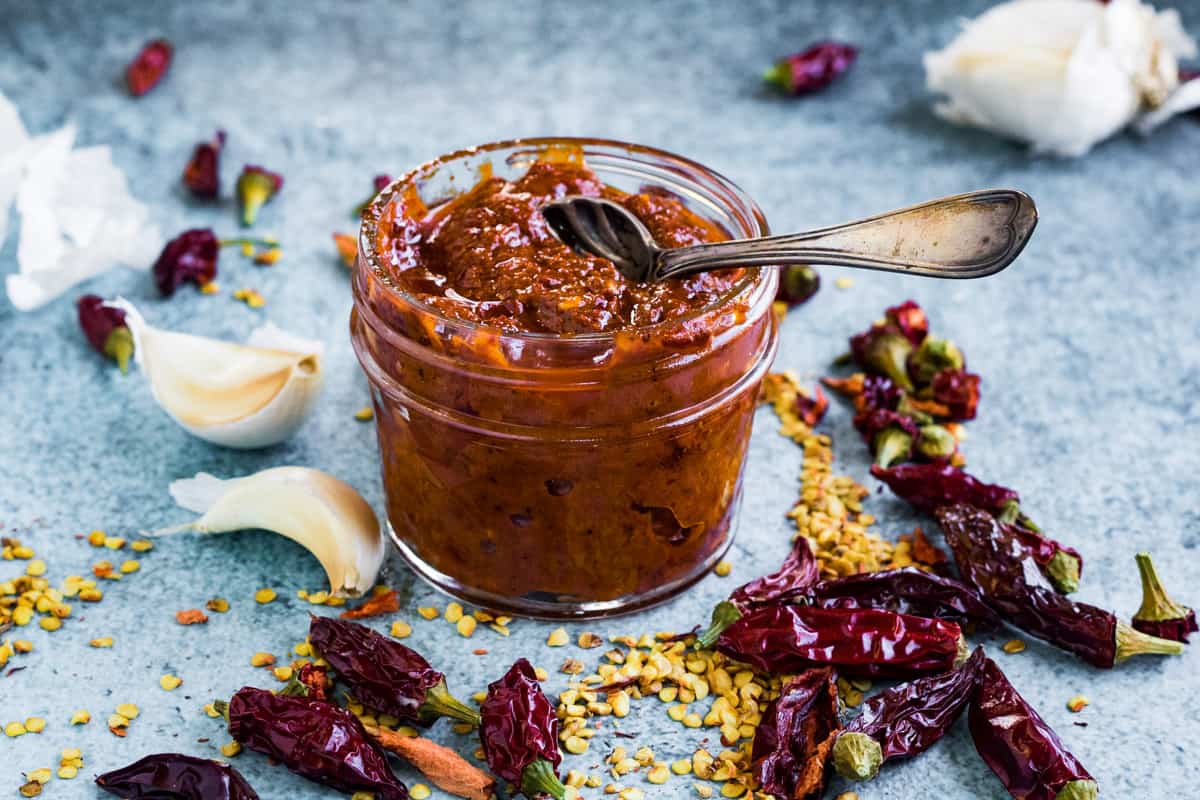 Harissa paste in a canning jar with ingredients scattered around the table.