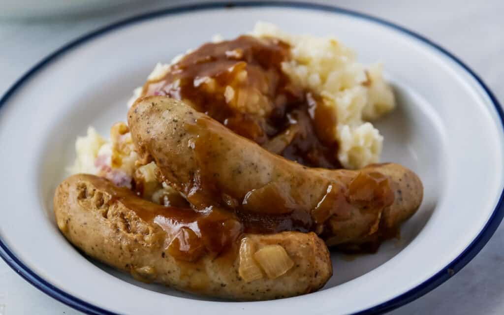 Sausages with onion gravy on top of mashed potatoes.