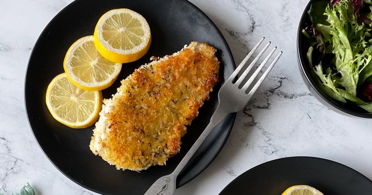 Italian Chicken Cutlets with lemon slices on black plate with fork