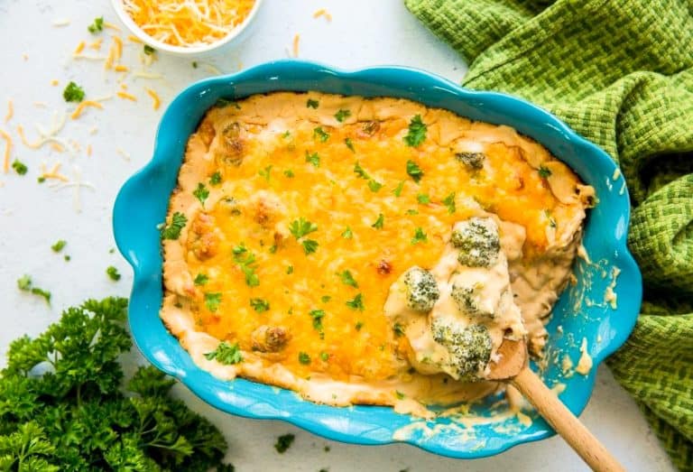 Keto Broccoli Cheese Casserole in a blue casserole dish with a wooden spoon and green napkin