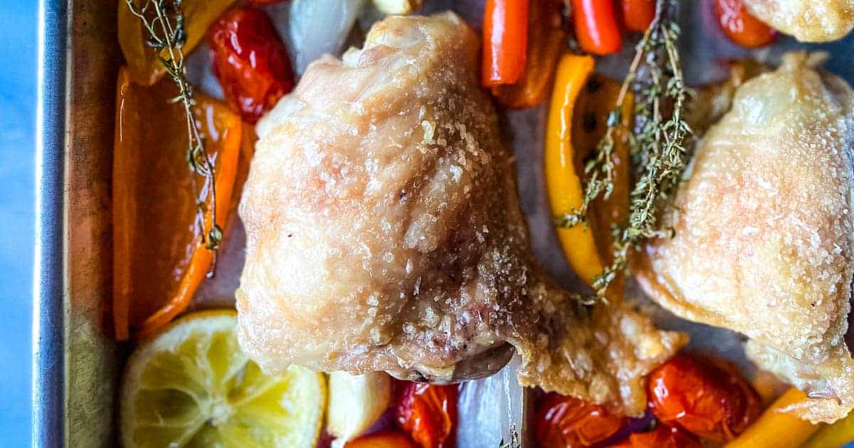 Lemon chicken with peppers, onions and tomatoes on a baking sheet.