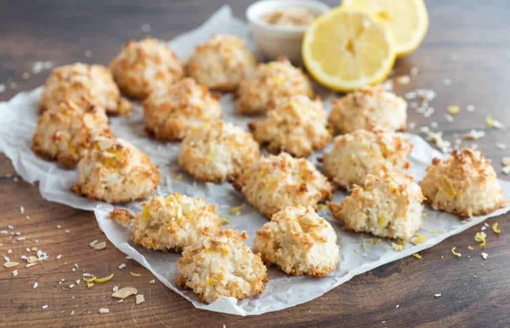 Lemon coconut macaroons on a sheet of parchment paper on top of a wooden table.