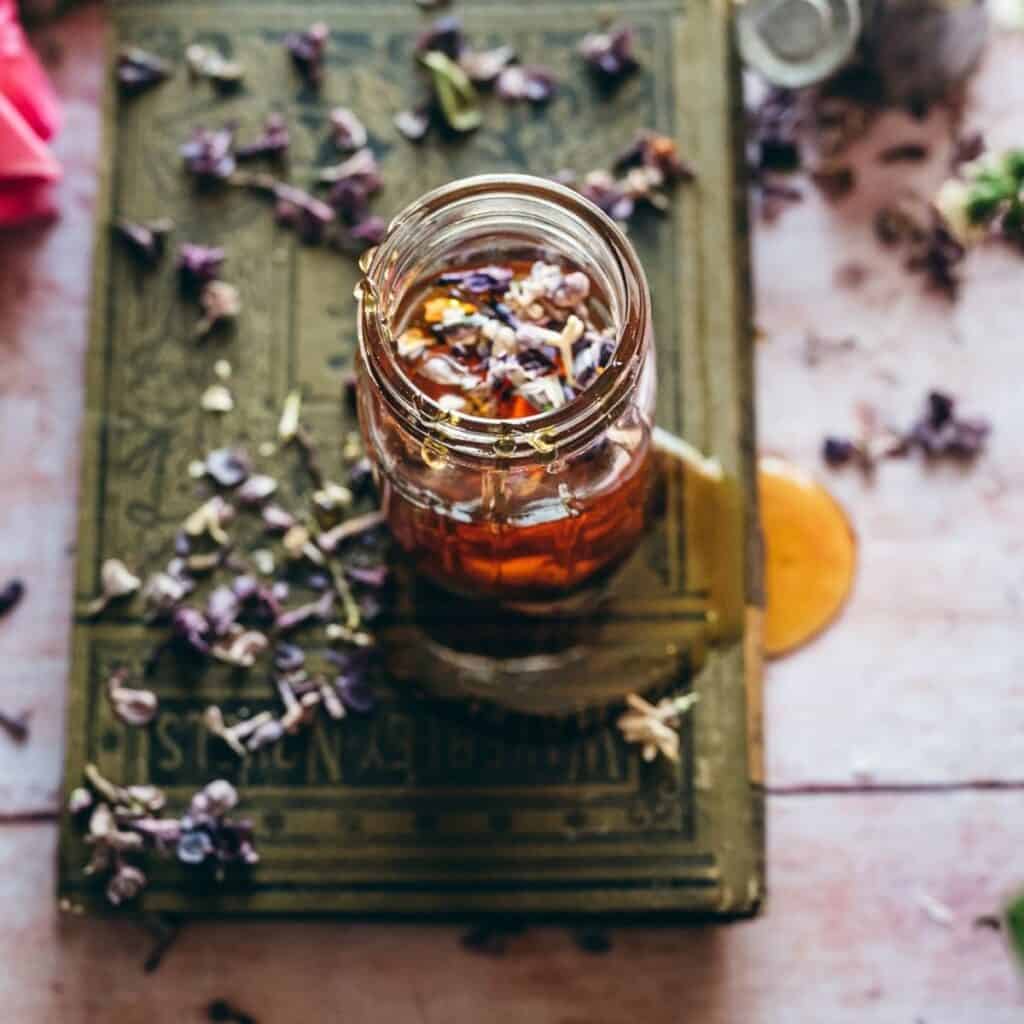 A clear jar filled with honey and scattered with edible flowers.