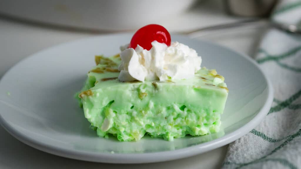 Piece of lime jello salad topped with whipped cream and a cherry.