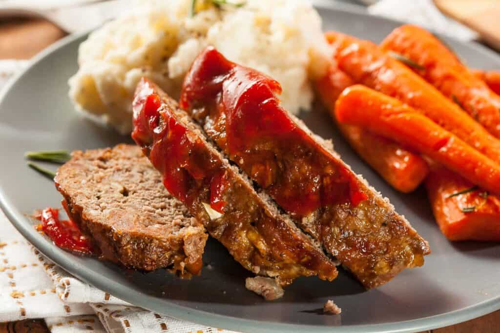 Slices of meatloaf on a plate with mashed potatoes and carrots.