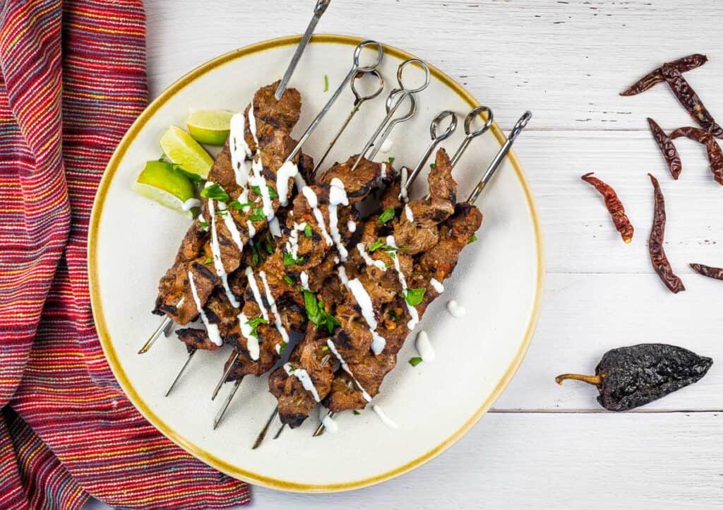 Grilled Steak skewers on a white plate with chilis nearby.