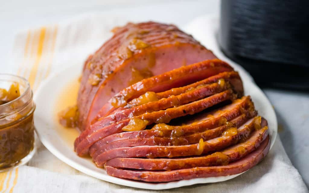 Sliced ham with peach glaze in front of air fryer.