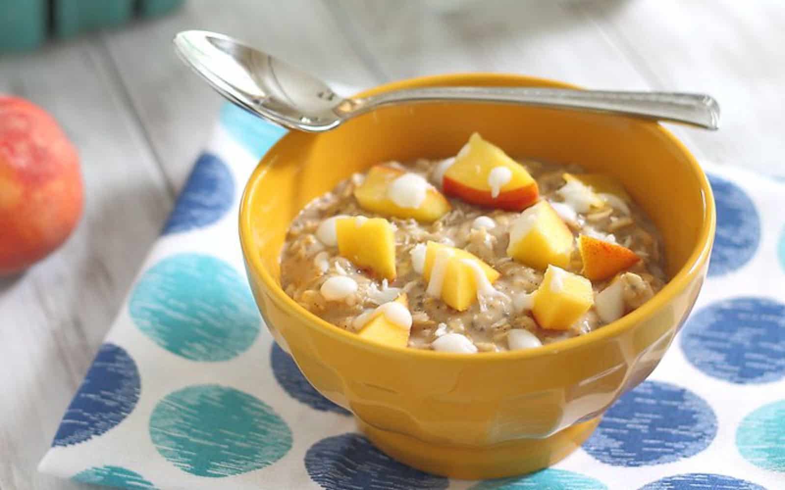 Peaches and cream oatmeal topped with chopped peaches and coconut cream drizzle in a yellow bowl.
