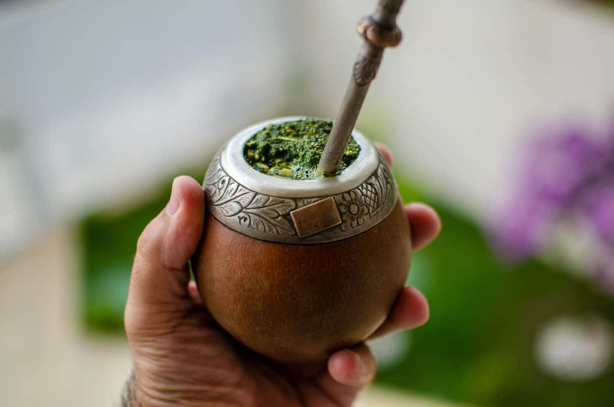 Holding a cup of Yerba tea with spoon inside.