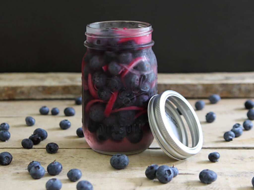 Quick pickled blueberries and red onions in a mason jar on wooden surface.