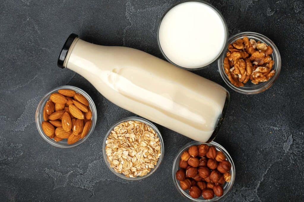 Overhead shot of a bottle of plant-based milk with bowls of nuts and oats.