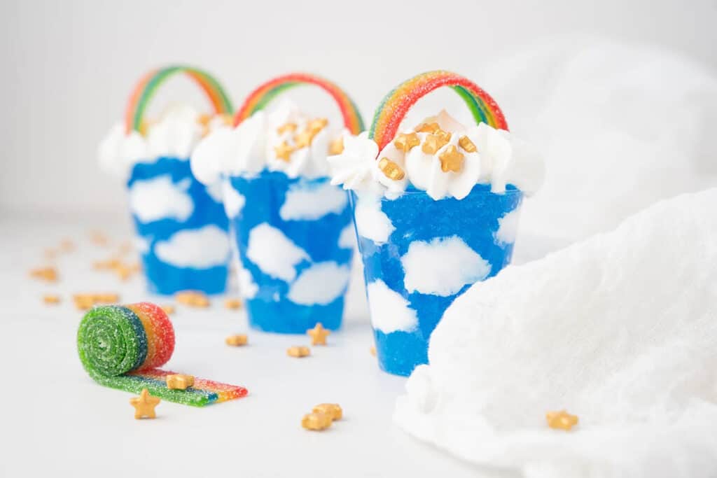 A shooter with blue jello that looks like it has clouds in it. There is a rainbow candy on top.