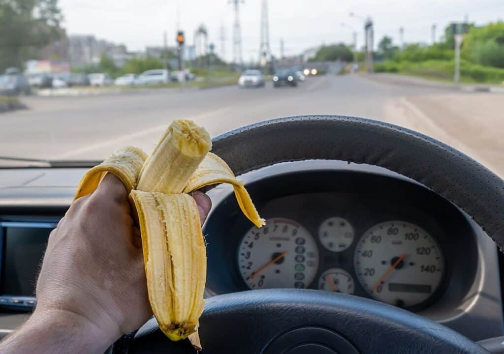 Driver eating a banana while driving on a road trip.