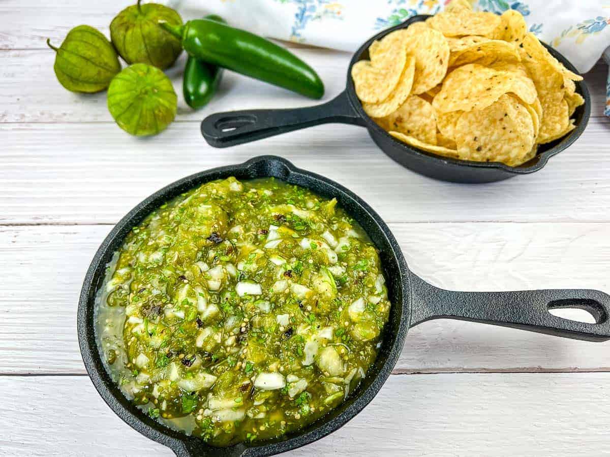 Roasted Tomatillo Salsa in a black pan with tortilla chips in a second pan.