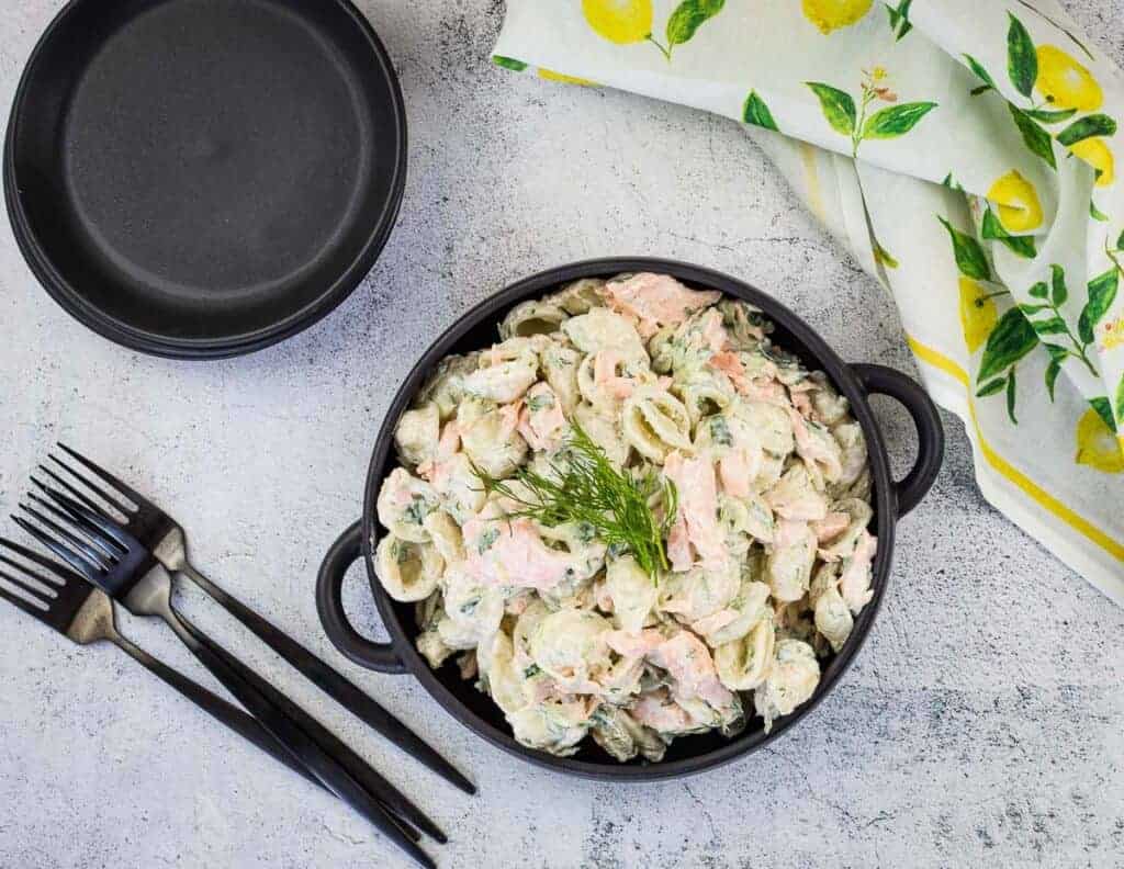 Salmon pasta salad in a black bowl with forks nearby.