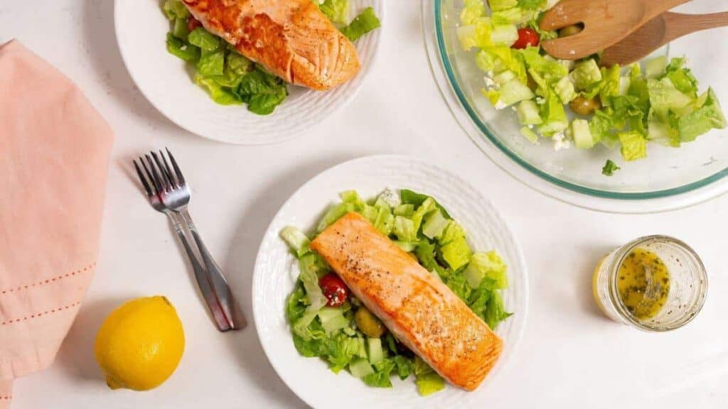 White plates with salad greens and salmon.
