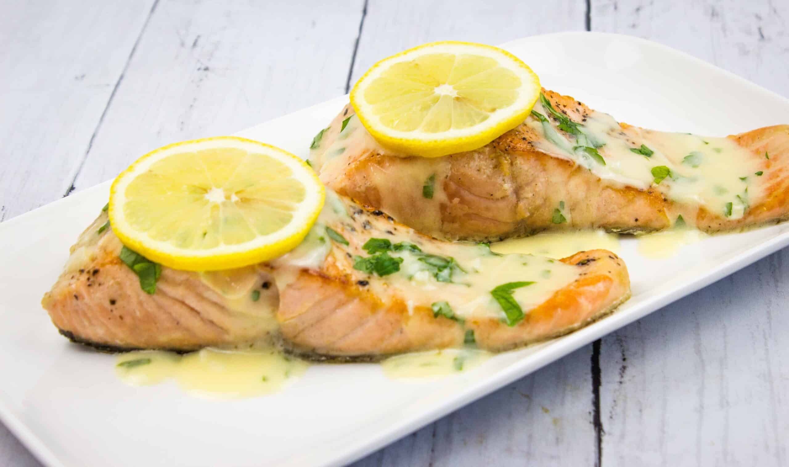 Two salmon fillets with lemon sauce on a white plate.