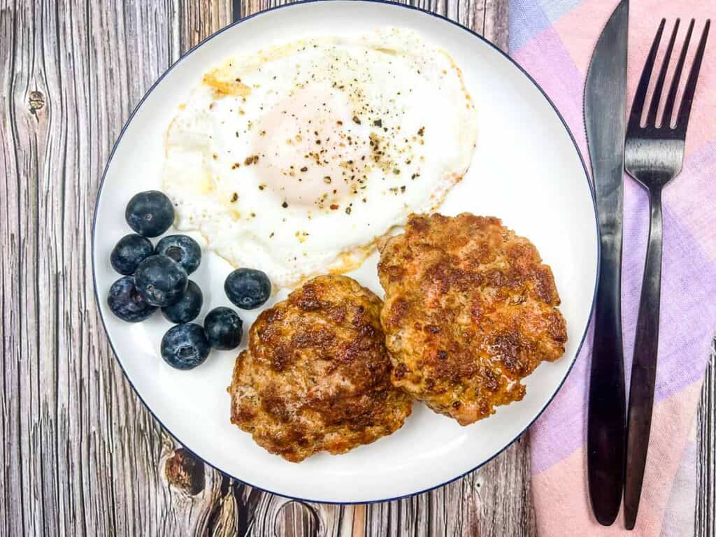 Breakfast Sausage Patties on a plate with a fried egg and blueberries.
