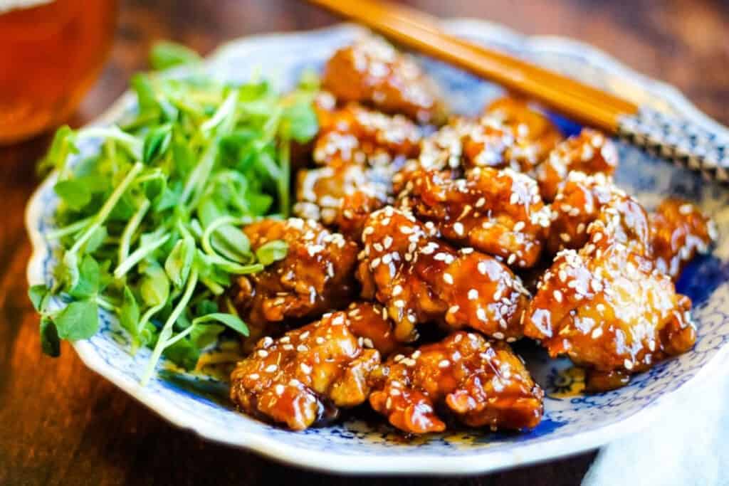 Sesame chicken on a blue and white plate with pea shoots.
