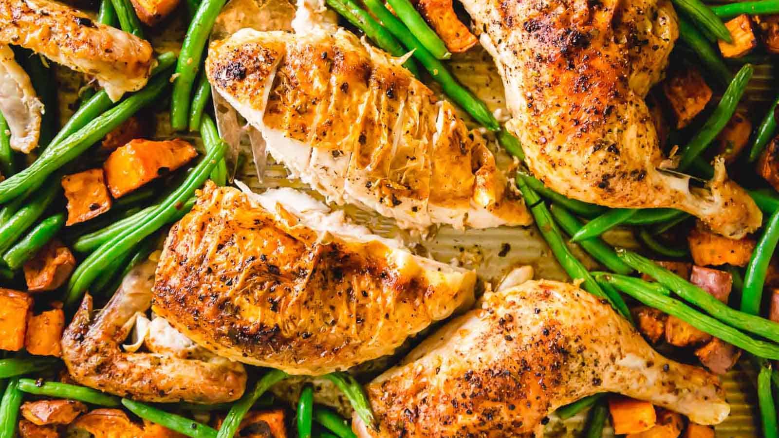 Spatchcock chicken with peri peri seasoning on a baking sheet with green beans and sweet potatoes.