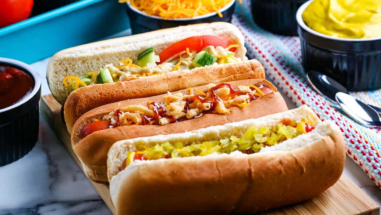 Three crock pot hot dogs with assorted toppings.