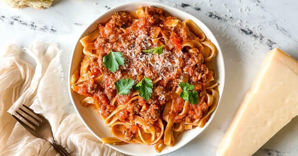 Slow cooker lamb ragu on a plate with a wedge of parmesan on the side.