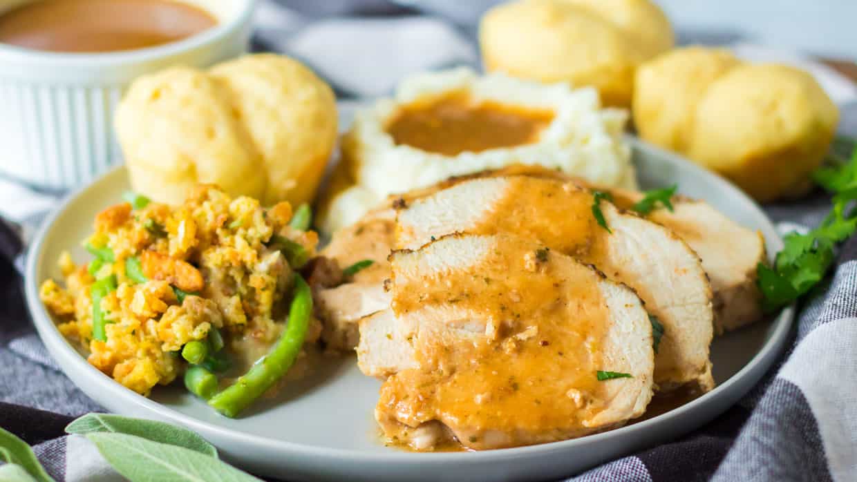 Slow Cooker Turkey Breast on a plate with gravy, stuffing, mashed potatoes and a roll.
