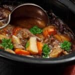 A close-up of beef stew with carrots, potatoes, and parsley in a black slow cooker, with a metal ladle resting inside—perfect for showcasing the hearty meals you can create with slow cookers.