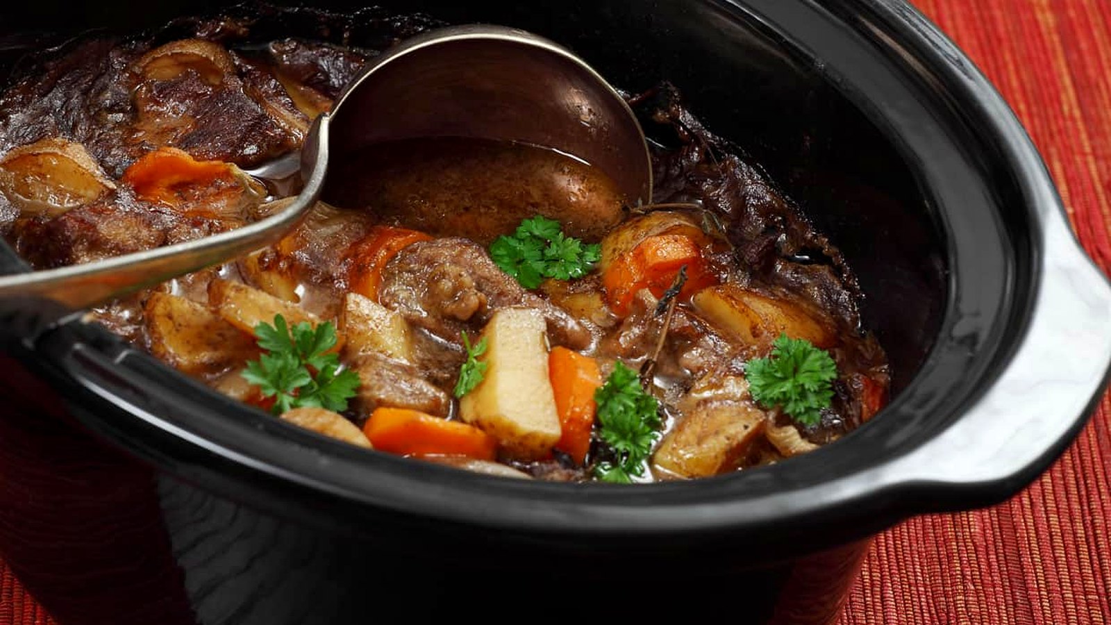A close-up of beef stew with carrots, potatoes, and parsley in a black slow cooker, with a metal ladle resting inside—perfect for showcasing the hearty meals you can create with slow cookers.