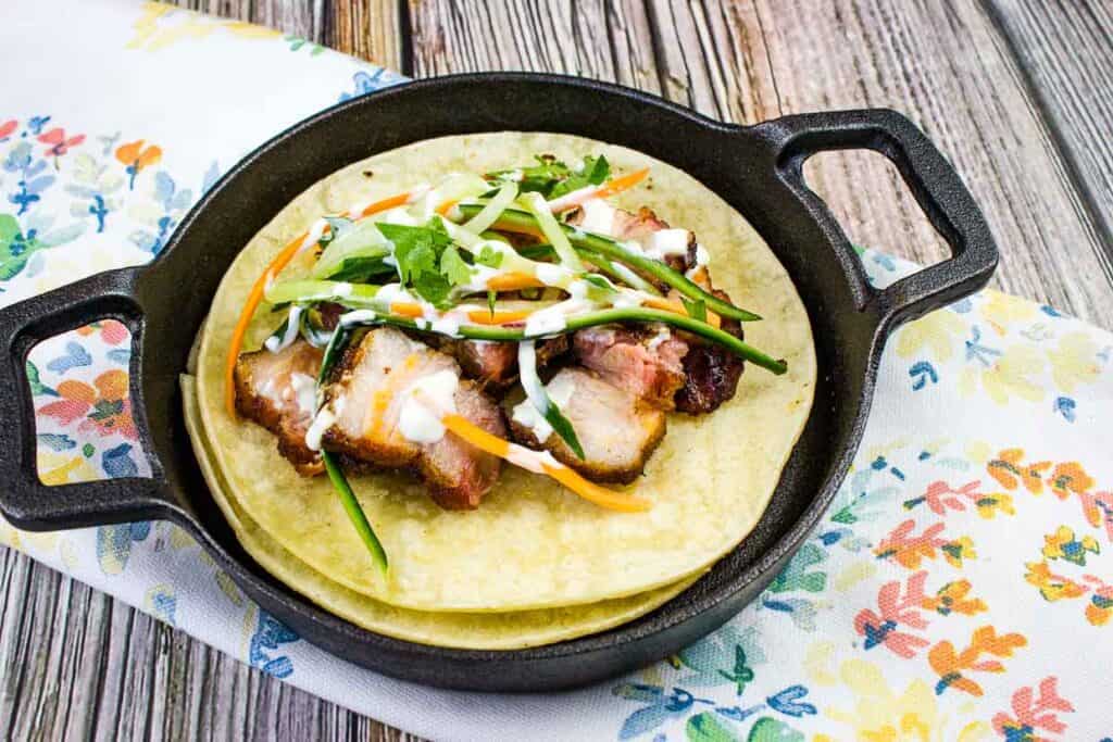 Smoked pork belly tacos on a black plate.