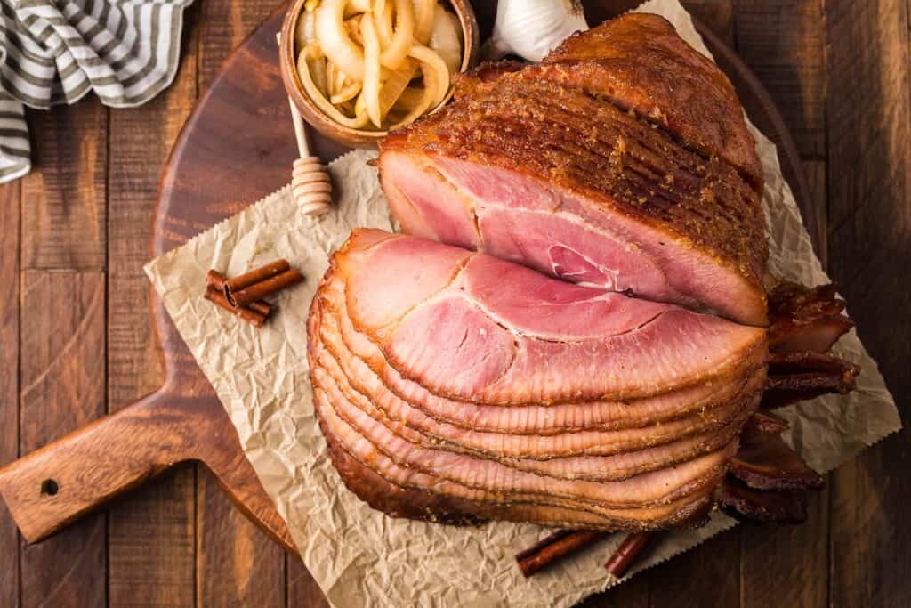 A smoked ham cut into slices on a cutting board.