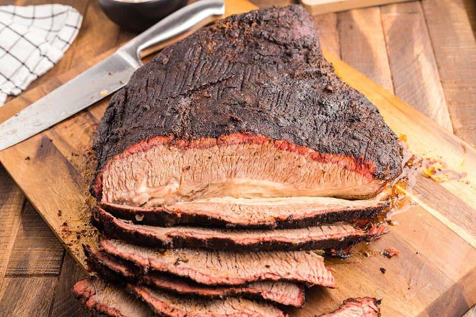 A smoked brisket on a cutting board being cut into slices.