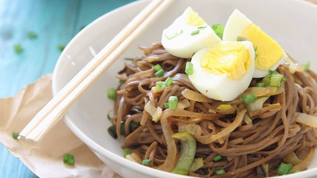 Soba noodles in a bowl with green onions, leeks and hard boiled egg.