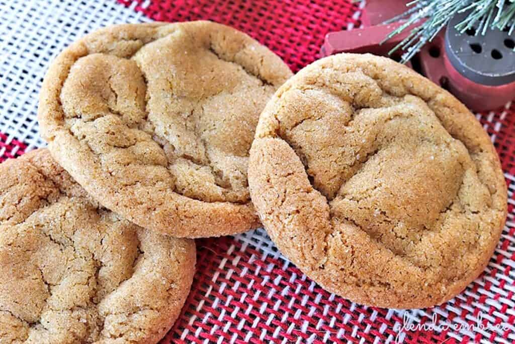 Three stacked Soft Chewy Ginger Cookies on a red and white checked burlap cloth next to a Christmas tree ornament.