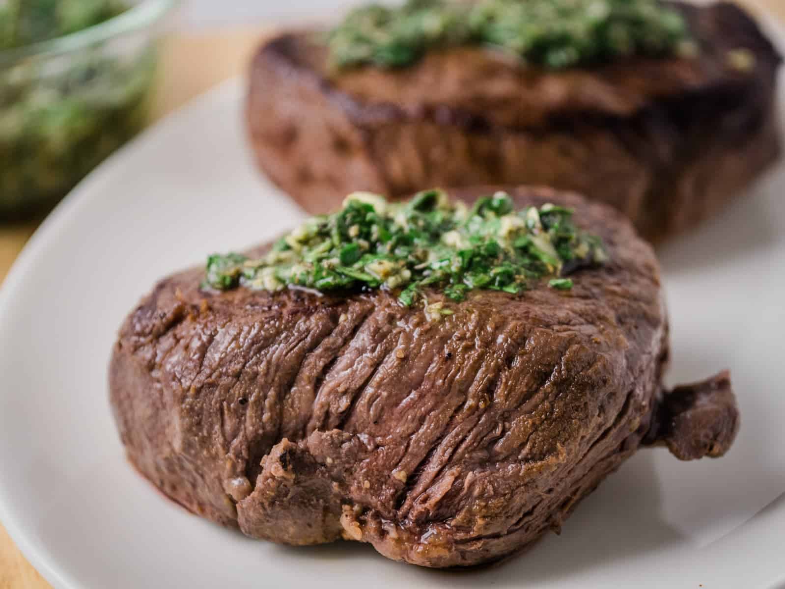 Two steaks with pesto sauce on a plate.