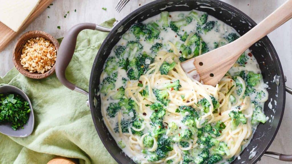 Spaghetti alfredo with broccoli florets in a pot with wooden spoon.