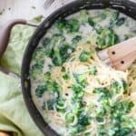 Spaghetti alfredo with broccoli florets in a pot with wooden spoon.