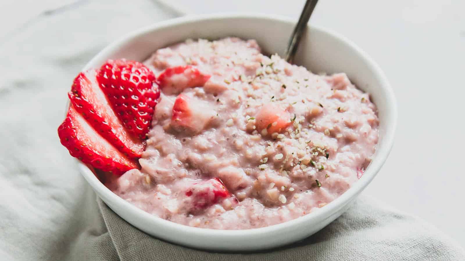 Strawberries and cream oatmeal garnished with fresh strawberry slices in a bowl with a spoon.
