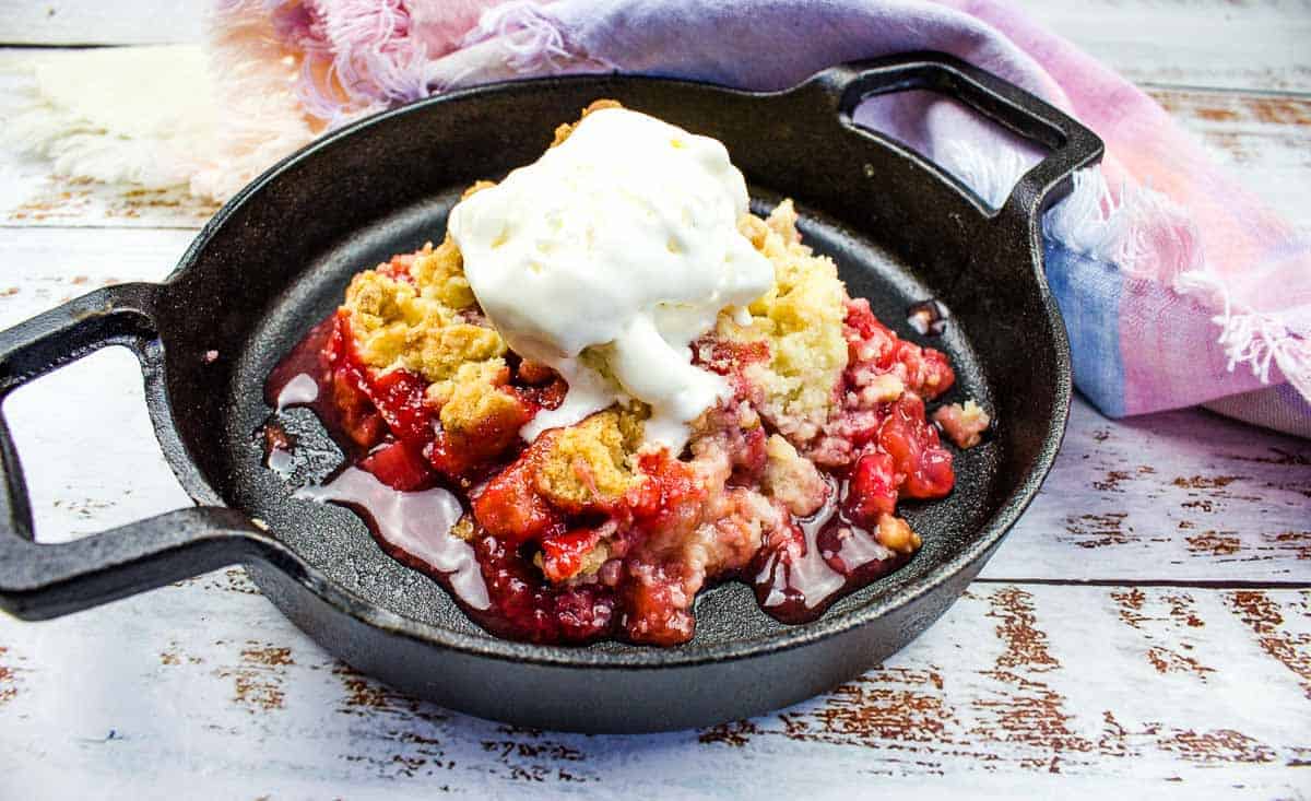 Strawberry Rhubarb Crumble in cast iron with vanilla ice cream on top.