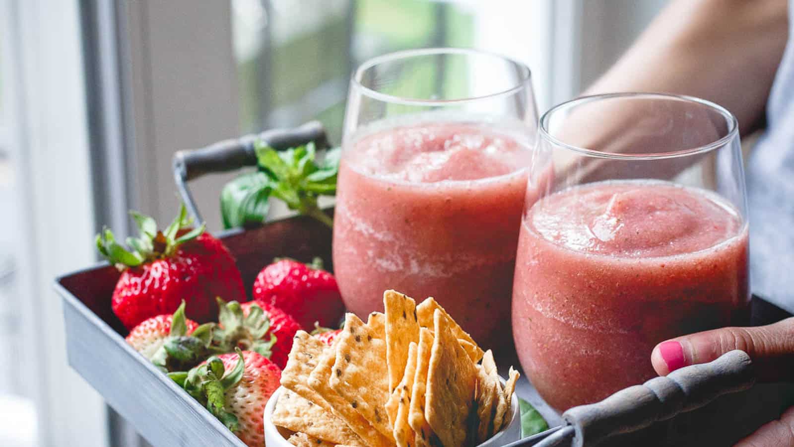 Strawberry slushies on a tray with fresh strawberries and crackers.